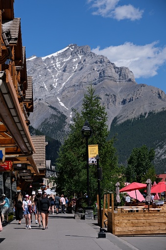 Banff, Canada – July 22, 2022: A group of adults walking down a street with towering mountains in the background, illuminated by a clear blue sky, Banff Alberta