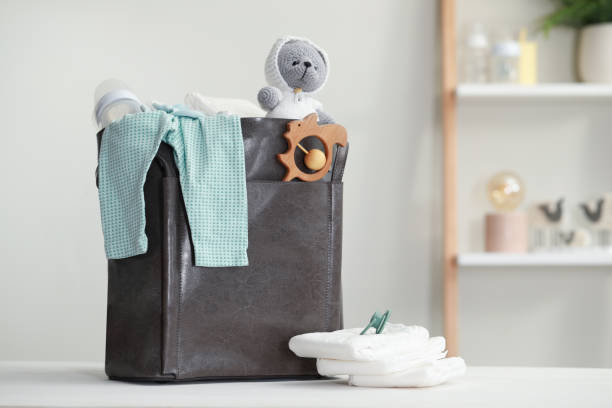 istock Mother's bag with baby's stuff on white wooden table indoors. Space for text 1795377557