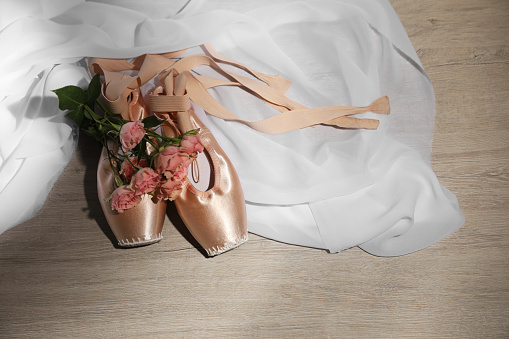 Ballet shoes. Elegant pointes and bouquet of roses on wooden floor, space for text