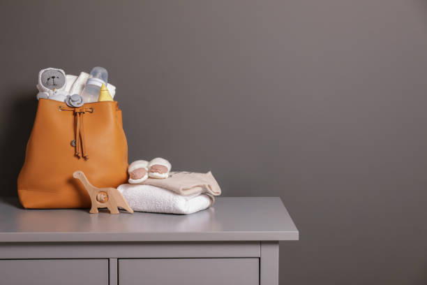 灰色の壁の近くの箪笥の上に赤ちゃんのものが入った母親のバッグ、テキスト用のスペース