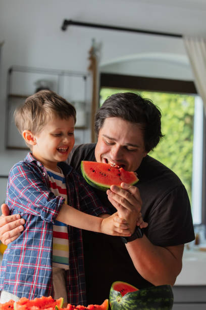 istock Father and son eating watermelon in kitchen 1795382565