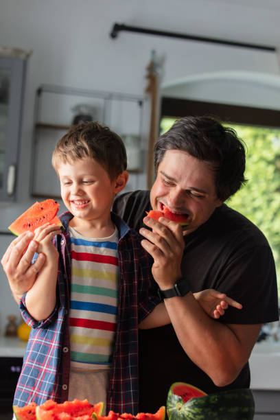istock Father and son eating watermelon in kitchen 1795382661