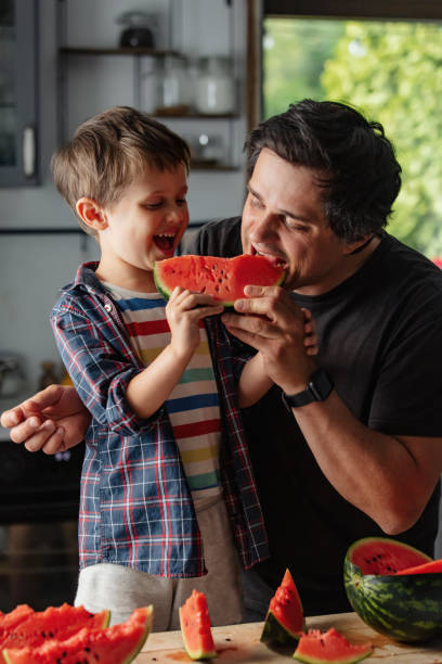 Father and son eating watermelon in kitchen