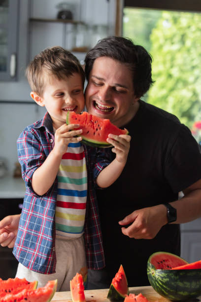 istock Father and son eating watermelon in kitchen 1795382830