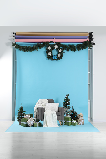 Beautiful Christmas themed photo zone with stylish armchair, trees and gift boxes in studio