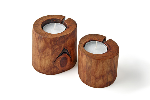 Two candles in wooden candlesticks from a tree trunk with a crack isolated on a white background.