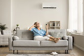 Happy relaxed senior lady holding AC remote control
