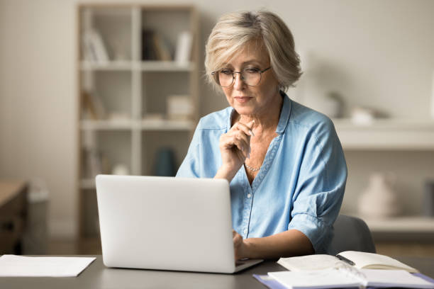 istock Serious elder senior freelance woman in glasses working at table 1795404363