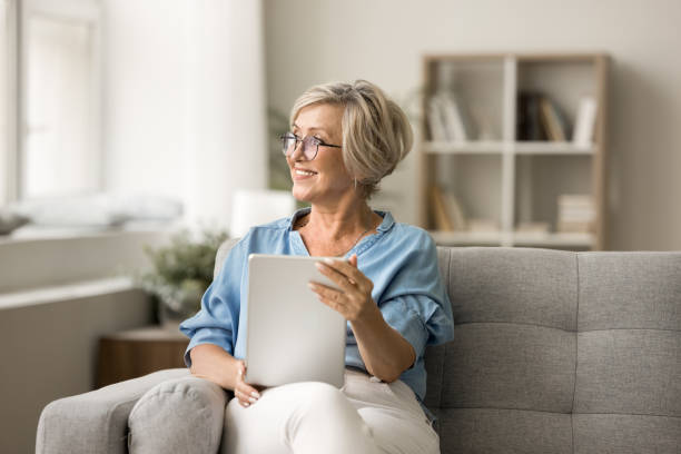 istock Happy thoughtful mature old woman using digital device at home 1795405496