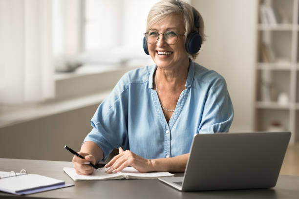 istock Cheerful pretty older student lady in headphones studying on Internet 1795409260