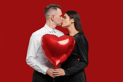 Lovely couple with heart shaped balloon kissing on red background. Valentine's day celebration