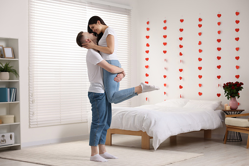 A senior couple is at home, they are embracing while holding a heart-shaped symbol