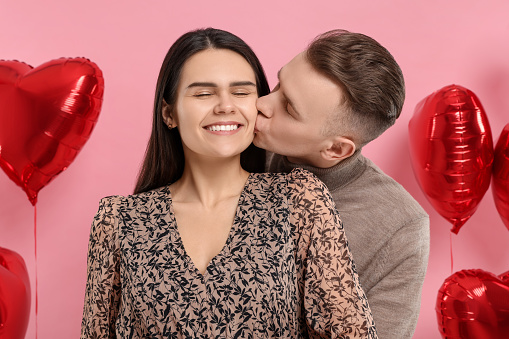 Boyfriend kissing his girlfriend on pink background. Valentine's day celebration