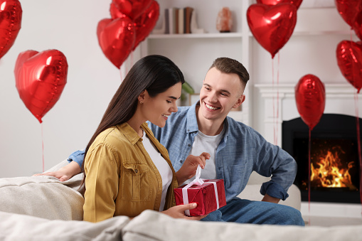 Woman opening gift from her boyfriend indoors. Valentine's day celebration