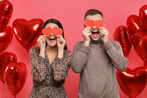 Lovely couple holding paper hearts near heart shaped air balloons on red background. Valentine's day celebration