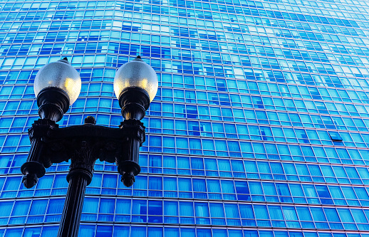 Close-up of a pole of vintage street lights against the blue glass exterior of a modern office building.