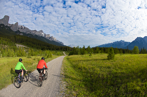 A man and woman go for a gravel road bike ride in the Rocky Mountains of Canada. Gravel bicycles are similar to road bikes but have sturdy wheels and tires for riding on rough terrain.
