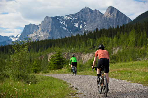 A man and woman go for a gravel road bike ride in the Rocky Mountains of Canada. Gravel bicycles are similar to road bikes but have sturdy wheels and tires for riding on rough terrain.