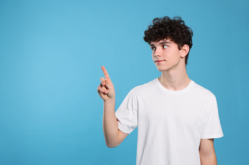 Teenage boy pointing at something on light blue background. Space for text
