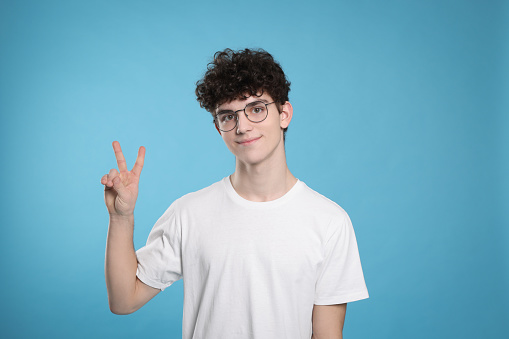 Happy young man wearing white t-shirt smiling at camera with thumb up, taking selfie. Studio shot, grey background.