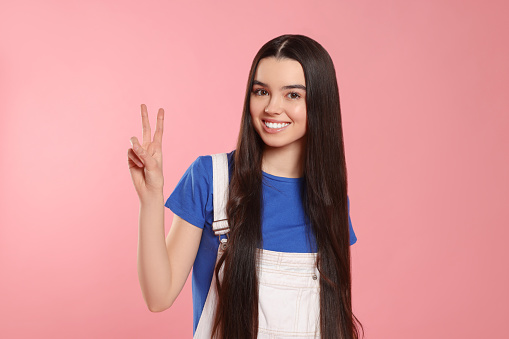 Teenage girl showing peace sign on pink background