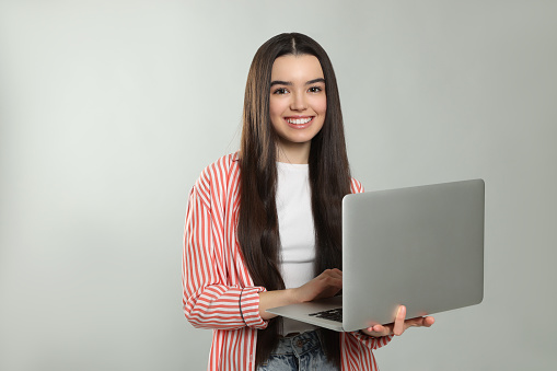 Teenage girl with laptop on light grey background