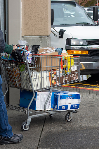 Tigard, OR, USA - Nov 6, 2023: A shopper walks out of the Costco store in Tigard, a suburban city in the Portland Metropolitan Area in Oregon, pushing a shopping cart filled with groceries, including food, milk, nutritional supplement and toiletries. As of 2023, Costco is the third largest retailer in the world.