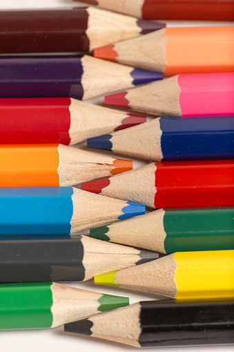 Color image depicting a close up macro view of a collection of colored pencils in a row, on a black background. Selective focus image with one of the pencils in sharp focus with the others blurred out of focus.