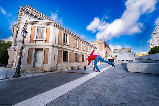 In the urban heart of Madrid, a red-clad, bearded parkour enthusiast flips gracefully.
