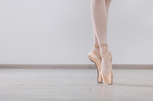 Young ballerina in pointe shoes practicing dance moves at studio, closeup. Space for text