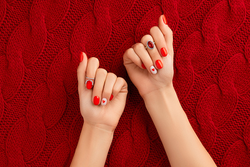 Manicured womans hands on knitted wool red fabric. Fashionable valentines day nail design
