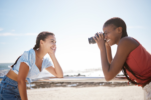 Summer, photographer and friends at a beach, having fun and posing for photograph on a sea trip together. Travel, happy and women bonding on a Florida vacation, relaxed and cheerful in with a camera