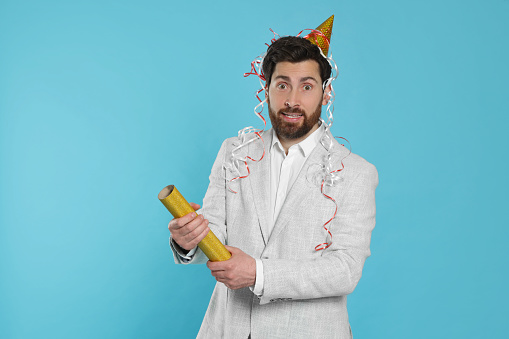 Confused man with party popper on light blue background