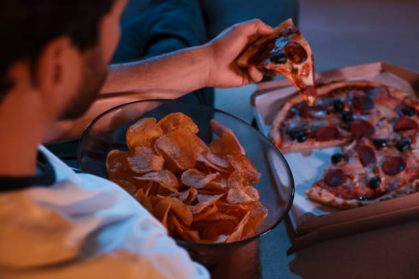 istock Man eating chips and pizza while watching TV on sofa at night, closeup. Bad habit 1795529662