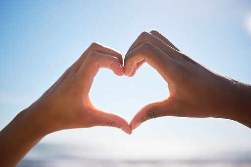 Heart sign, beach hands and blue sky on vacation by the sea, happy on international holiday in Miami and love for summer travel in nature. Person with emoji for happiness by the ocean in spring