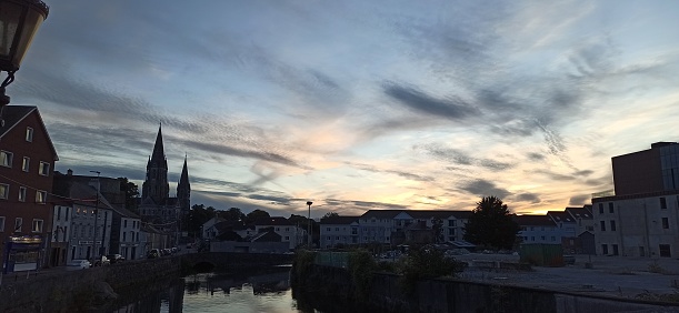 The sun dips behind St. Fin Barre's Cathedral in Cork, painting the sky with dramatic evening colors.