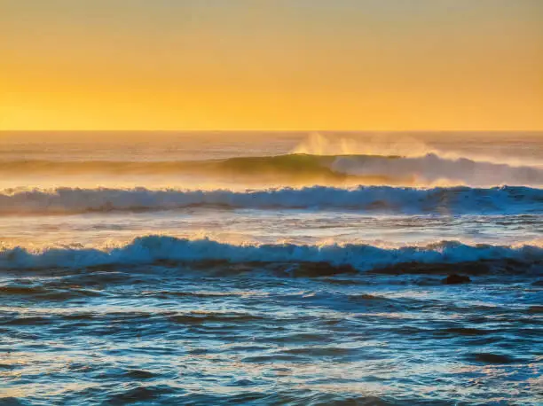 Large, dangerous incoming waves rolling into the coastline at sunrise or sunset