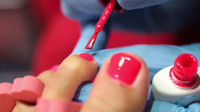 Manicurist applies red polish to client toenails