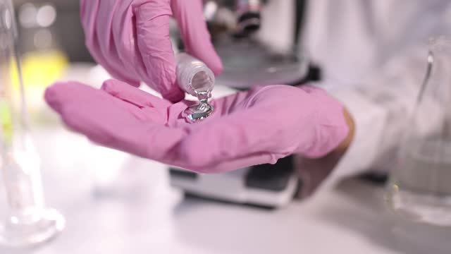 Scientist chemist in protective gloves pouring liquid metal into hand in laboratory closeup 4k movie slow motion