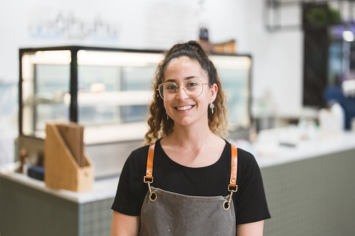 Confident female business owner wearing apron with positive emotions looking at camera.