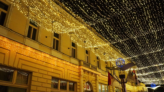 Sremsk Mitrovitsa, Serbia, December 26, 2022. Festive decoration of city streets. Garlands of yellow, white and gold lights and bulbs. Beautiful background for New Year, Christmas holiday