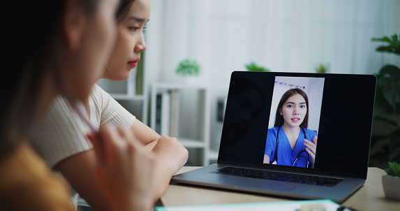 Selective focus on monitor during Two female teenage use laptop computer video call with young expert dentist while explains post brace or orthodontic care at home