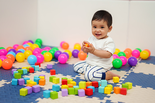 happy infant baby playing wooden block toy in playpen at home