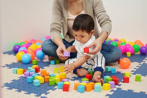 infant baby playing wooden block toy with mother in playpen at home