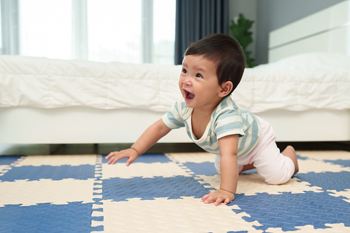 happy infant baby crawling on play mat or jigsaw floor in the bedroom