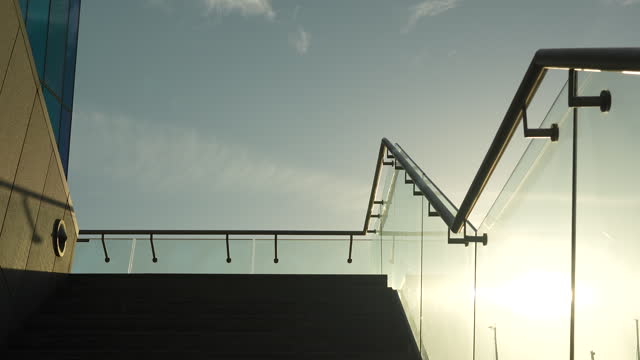Concrete staircase leading to glass balustrade against a sunlit sky with soft clouds.
