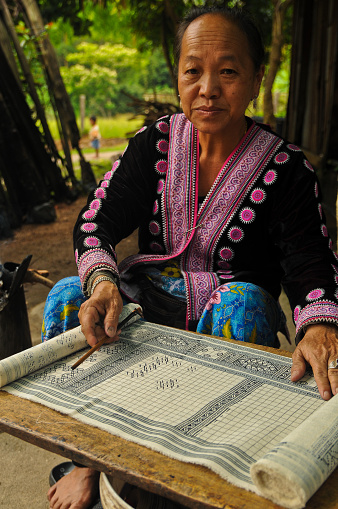 Close-up of a Hmong Tribe Woman demonstrating her Batik techniques & work in the Baan Tong Luang Hill-Tribe Village of Chiang Mai Province in Northern Thailand. There are a number of different tribes found in this village like the Karen, Palong and Hmong tribes. The Hmong tribe is originally from Mongolia-China and not  native to Thailand. These are refugees with limited rights. Many sell their handicrafts as a source of income. Photographed in May 2014.