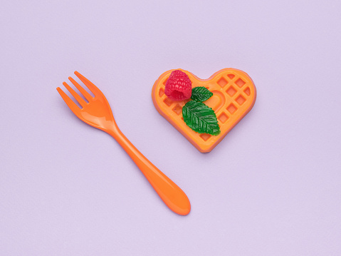 Orange plastic fork with a cookie figurine on a purple background. Creative dessert.