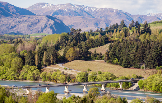 New Lower Shotover Bridge in Queenstown, New Zealand, arching over a serene river with a backdrop of mountains and trees. Part of the Queenstown trails.
