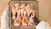 Chef hands wearing gloves pouring soy sauce  into a glass baking dish with chicken drumsticks in it. Marinated chicken drumsticks
